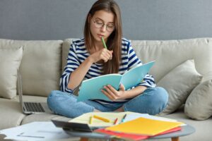 Female student preparing for dual course i n germany with books & laptop at home